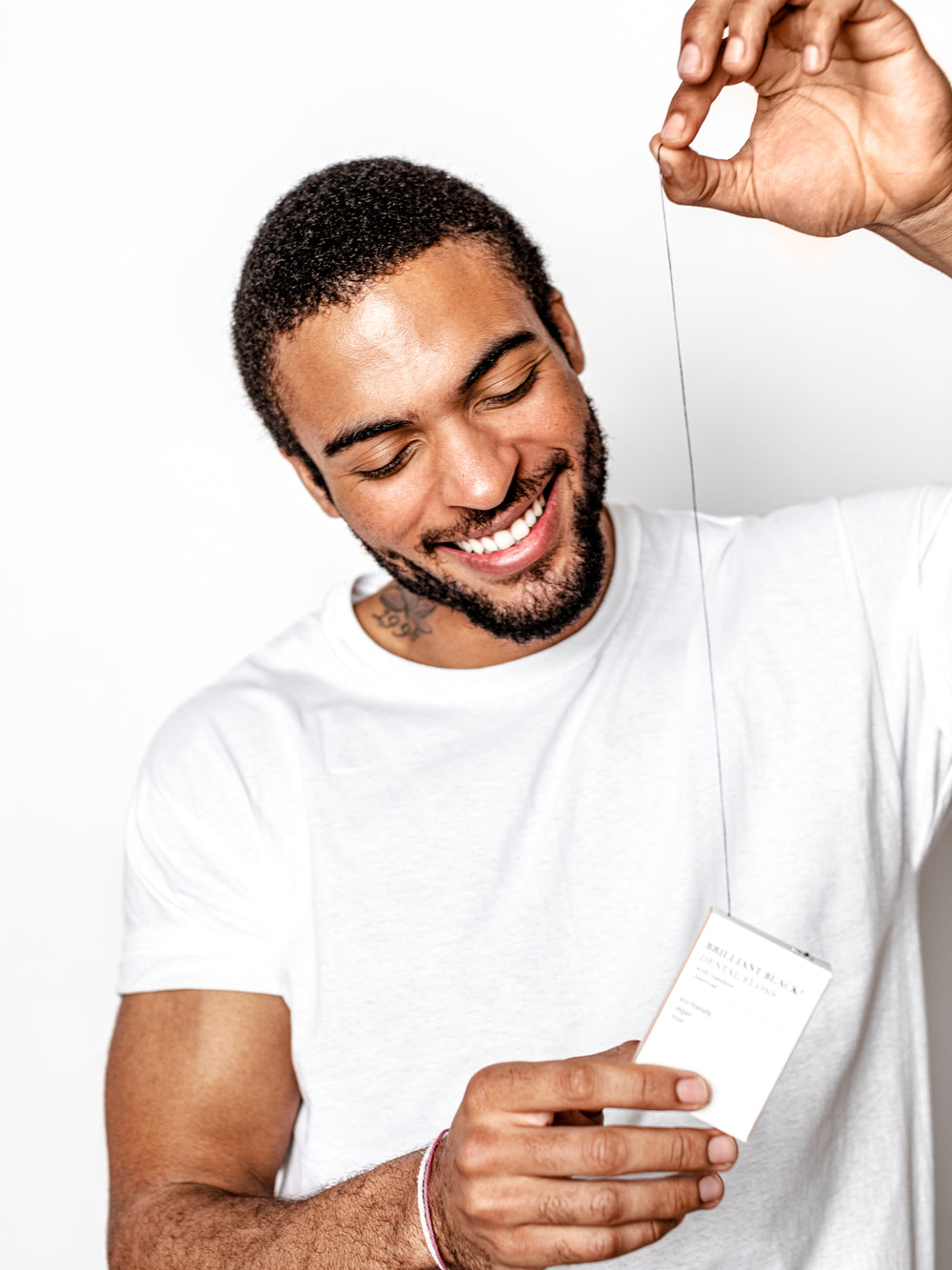 Man using Brilliant Black® dental floss to remove plaque and whiten between teeth with charcoal-infused bamboo floss
