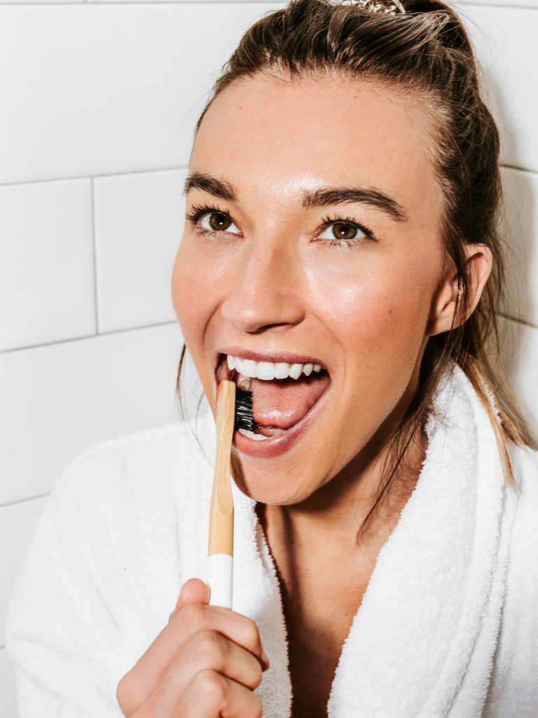 Woman brushing her teeth with Terra & Co.’s plant-based charcoal toothbrush, safe for sensitive gums and environmentally friendly
