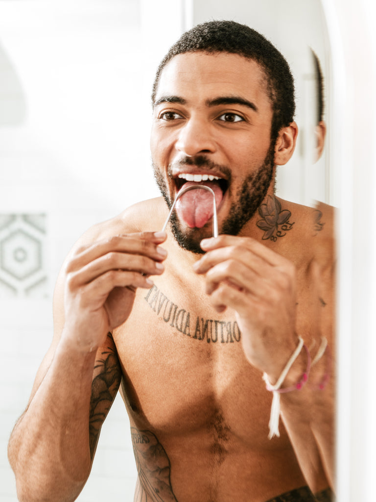 Man scraping tongue with Terra & Co. tongue cleaner to reduce bacteria, support digestion, and improve overall oral hygiene