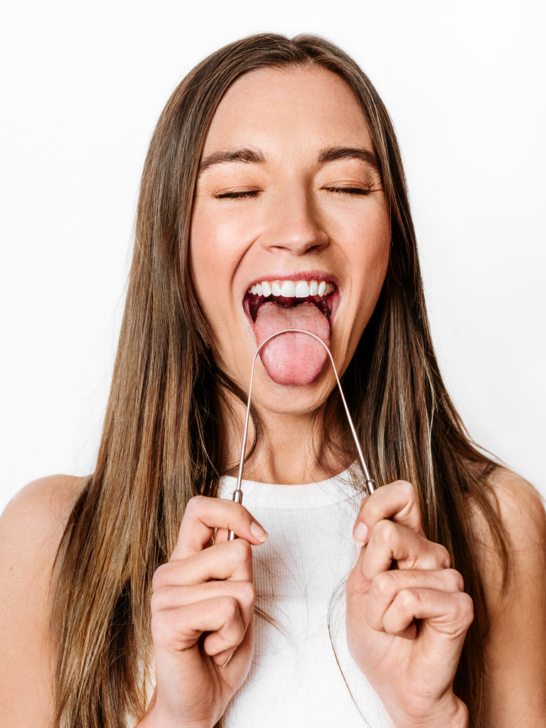 Woman using stainless steel tongue scraper as part of daily Ayurvedic oral hygiene routine for fresher breath and gut health